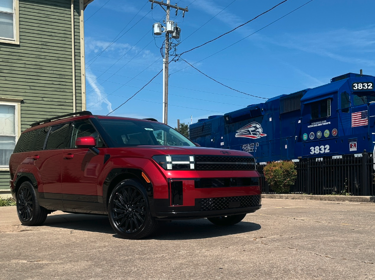 A red Hyundai SUV parked in front of a patriotic blue freight train in Fort Smith, Arkansas, under a clear fall sky.